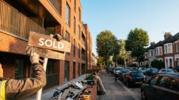 Red brick apartment building with sold sign, British urban street