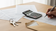 Calculator and tax papers beside house keys on a desk