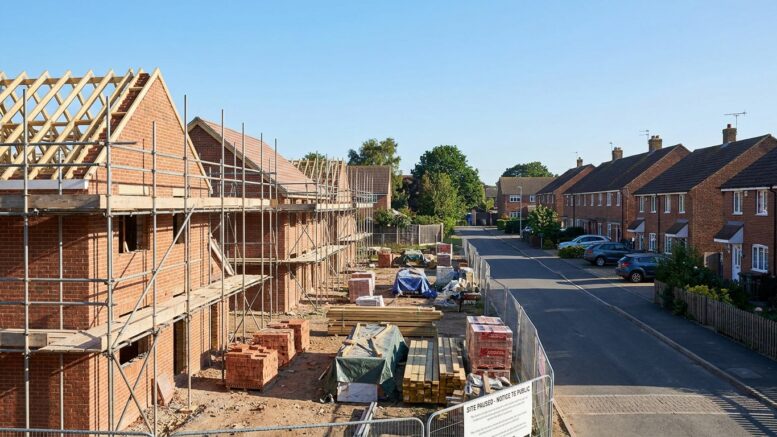 Half-built UK homes with scaffolding under clear blue sky