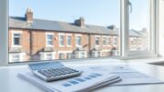 Calculator on UK landlord tax papers with terraced houses behind